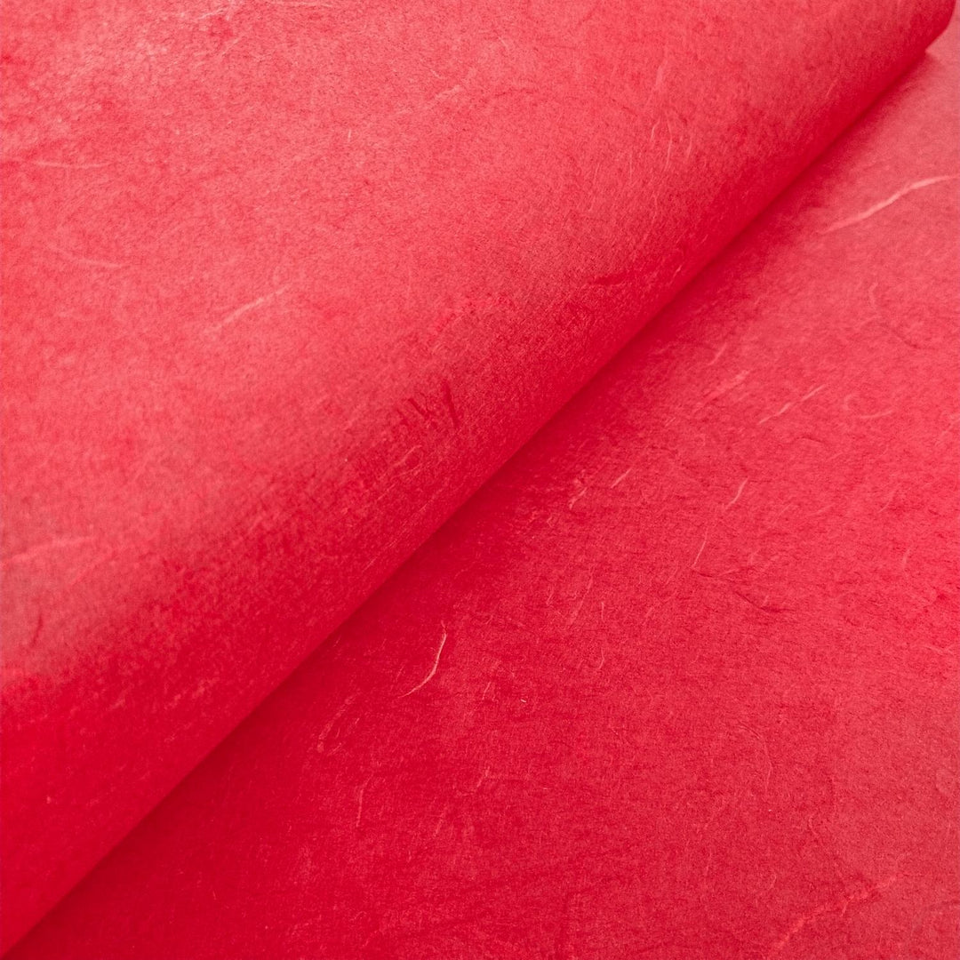 Textured cherry red mulberry paper from Kozo Studio captured in a close-up to reveal its organic handmade paper structure.