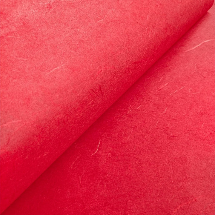 Textured cherry red mulberry paper from Kozo Studio captured in a close-up to reveal its organic handmade paper structure.