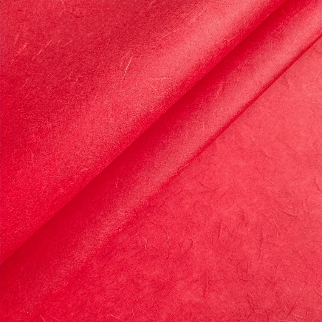 Close-up of cherry red Unryu mulberry paper from Kozo Studio highlighting handmade paper texture with dynamic folds and fibers.