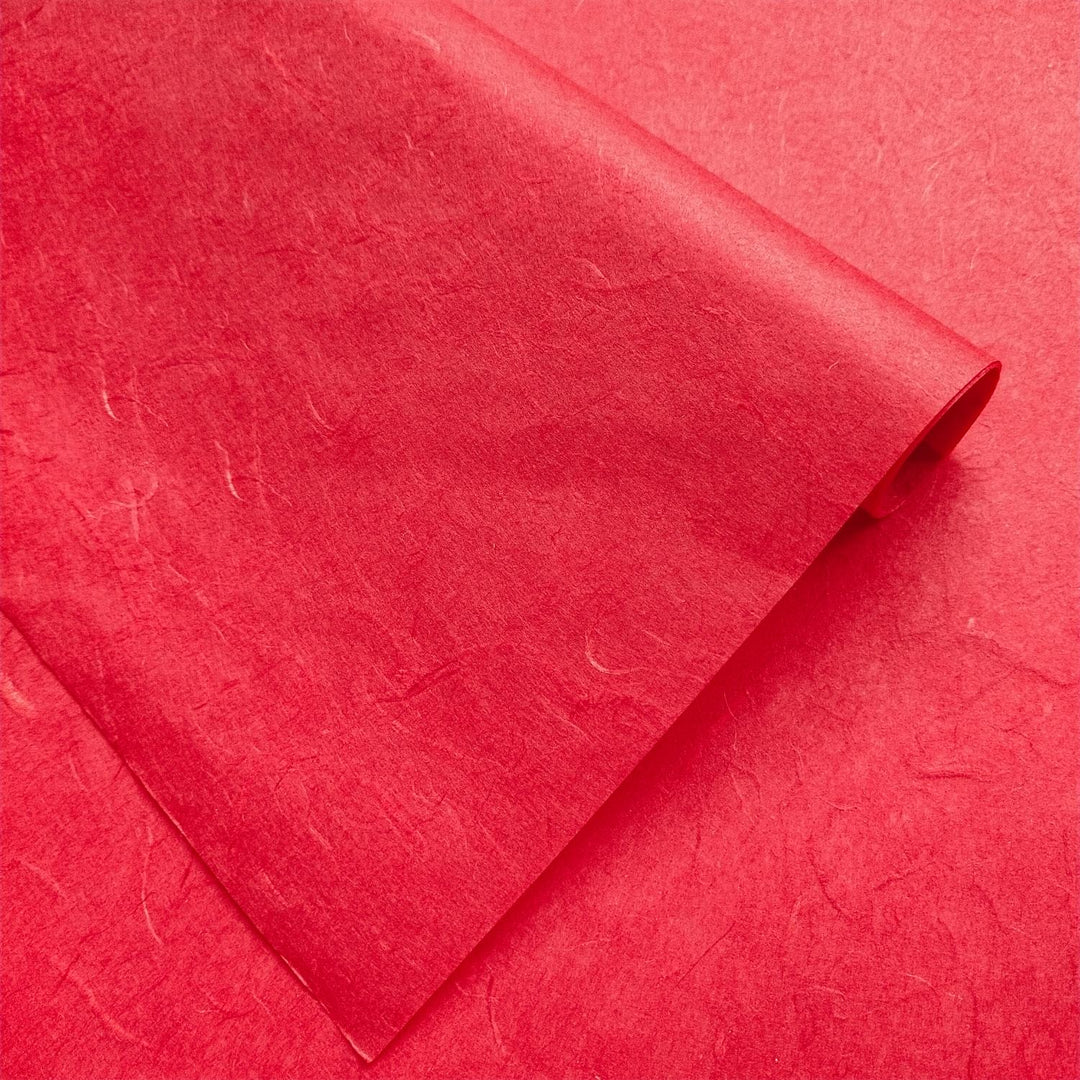 Handmade paper in cherry red by Kozo Studio showing textured mulberry fibers and diagonal creases for a natural look.
