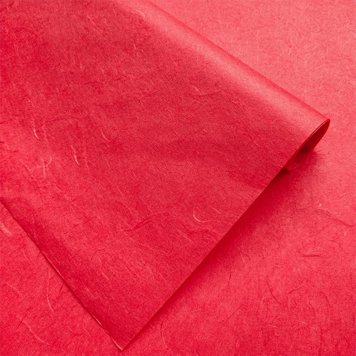 Handmade paper in cherry red by Kozo Studio showing textured mulberry fibers and diagonal creases for a natural look.