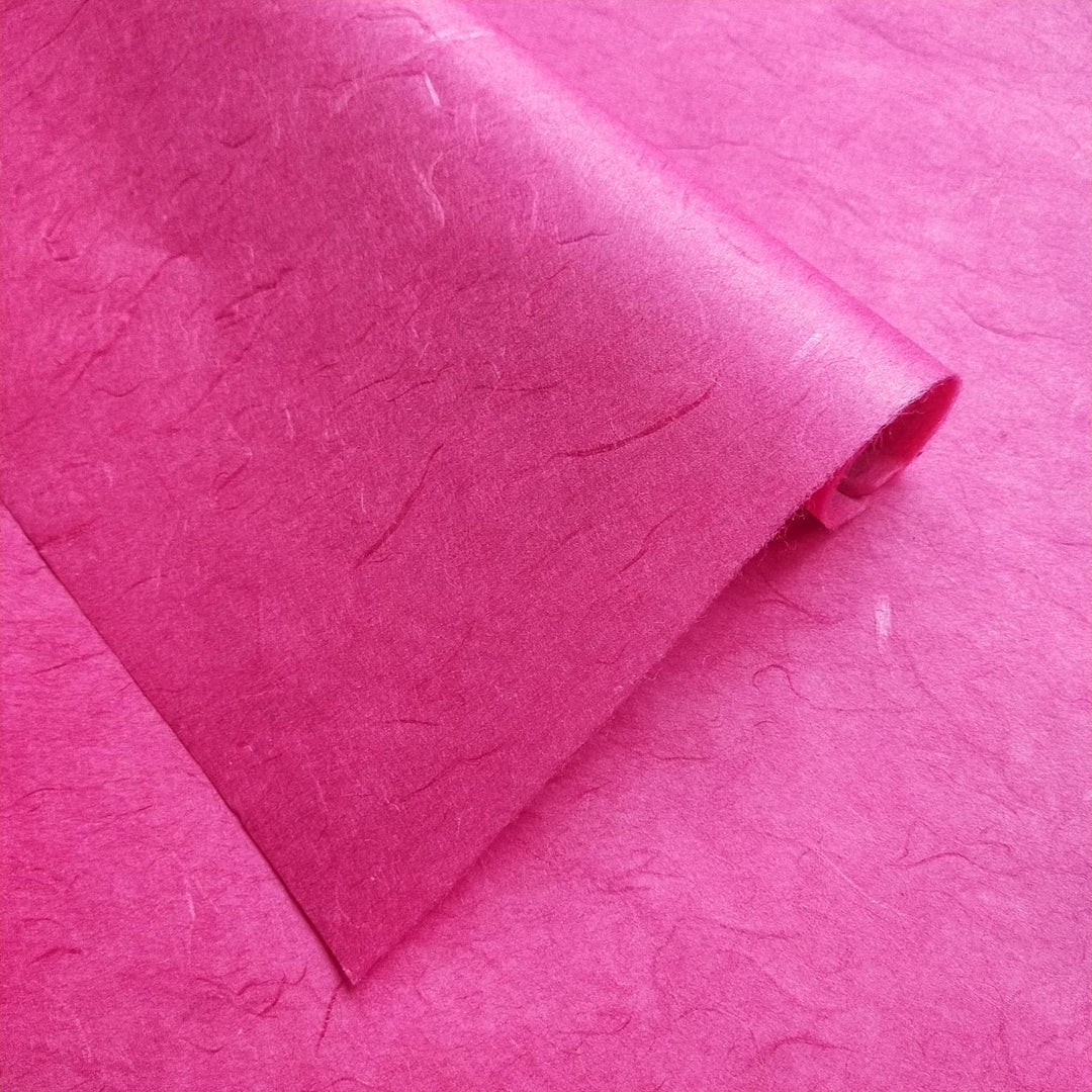 Close-up view of vivid fuchsia mulberry paper from Kozo Studio featuring a textured tread pattern and partial fold revealing both sides.