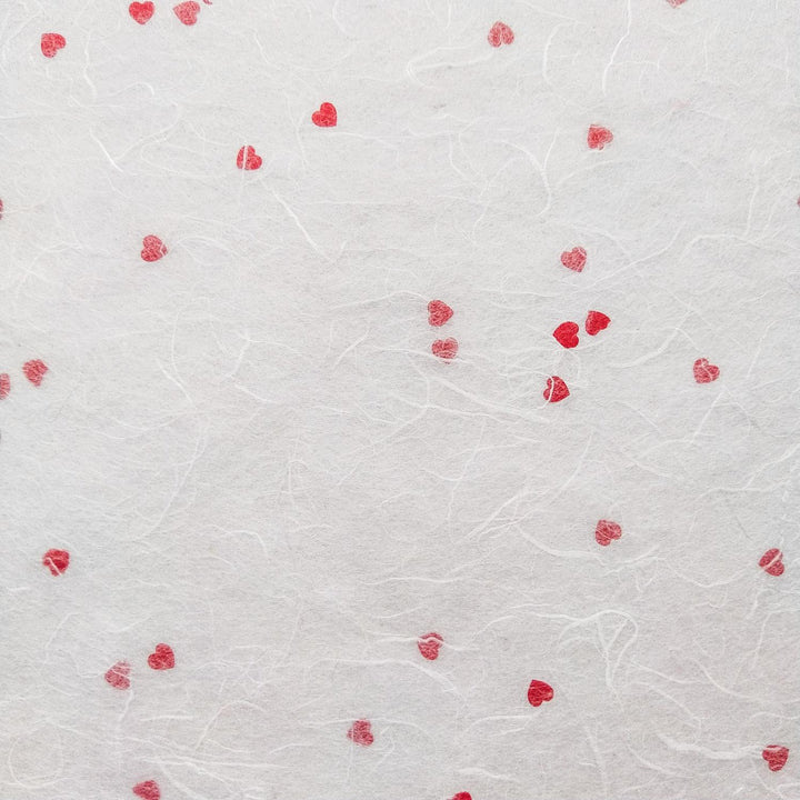 Textured mulberry paper with tiny red heart patterns created by Kozo Studio, a charming example of artisanal handmade paper.