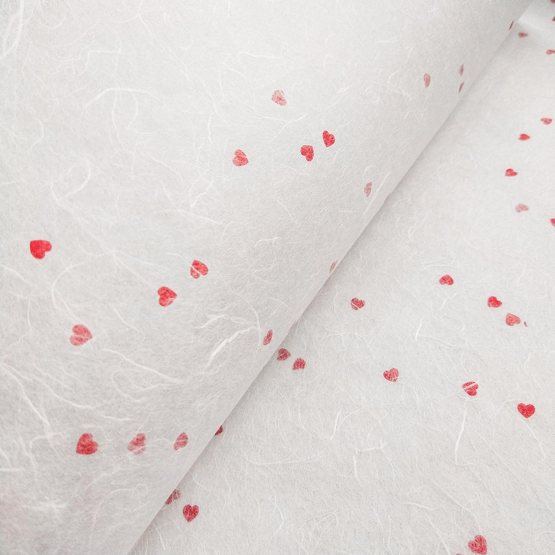 Close-up of white handmade mulberry paper with red heart embellishments by Kozo Studio, perfect for romantic crafts or stationery.
