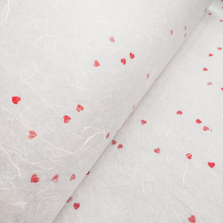 Close-up of white handmade mulberry paper with red heart embellishments by Kozo Studio, perfect for romantic crafts or stationery.
