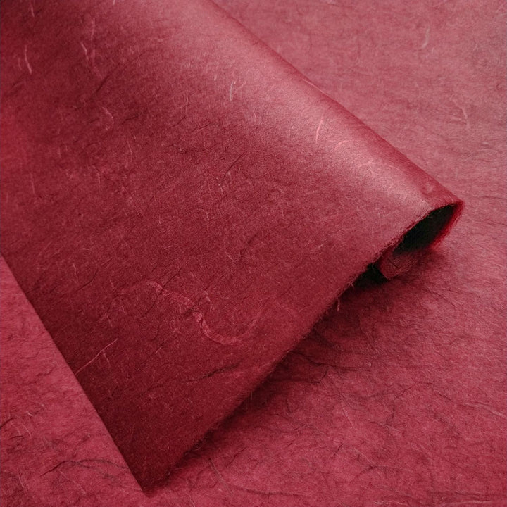 Handmade paper from Kozo Studio in a deep maroon hue, featuring Unryu Kozo texture with mulberry-like fibers and abstract layering.