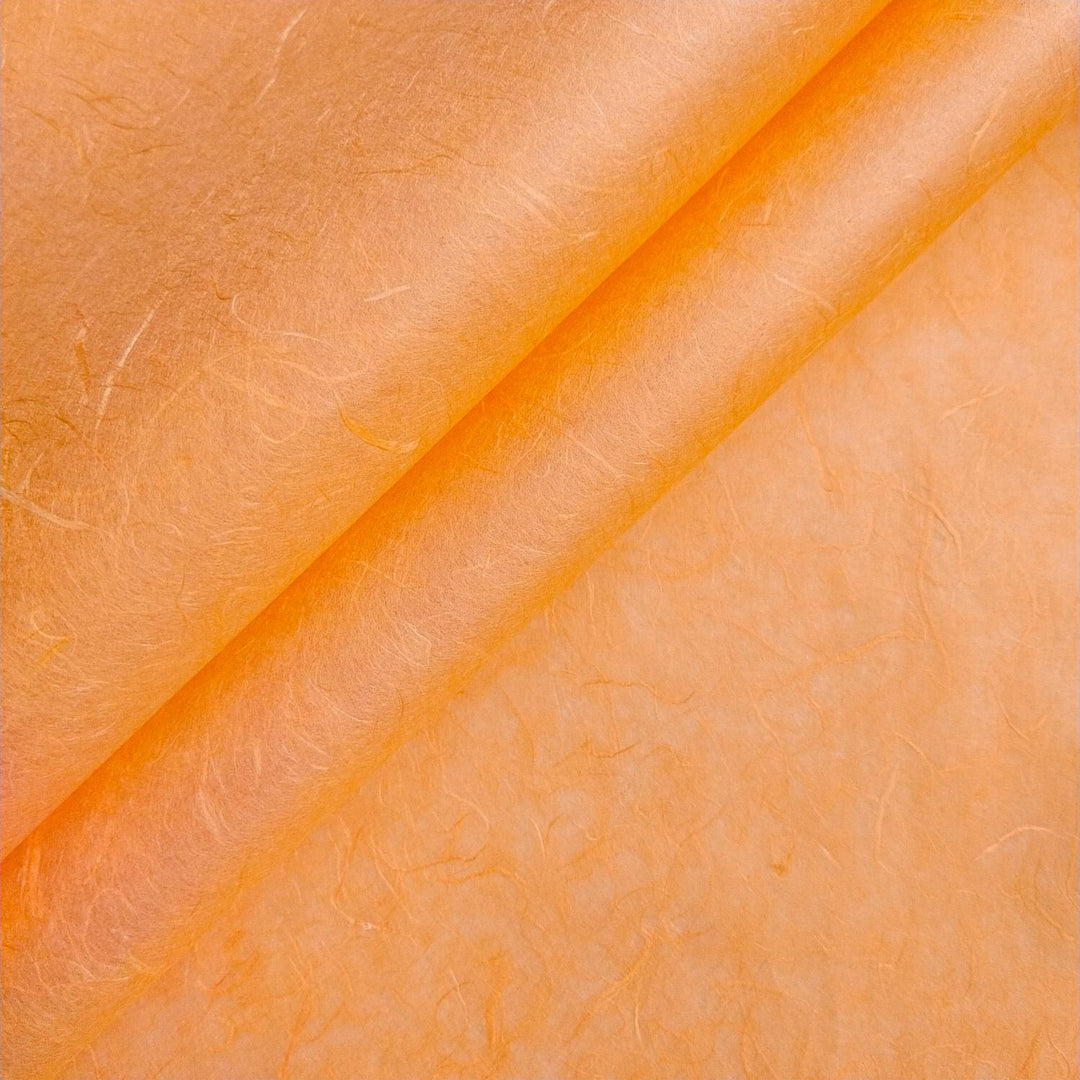 Close-up of handmade mulberry paper in tangerine orange by Kozo Studio, showcasing its fibrous texture and natural color variations.