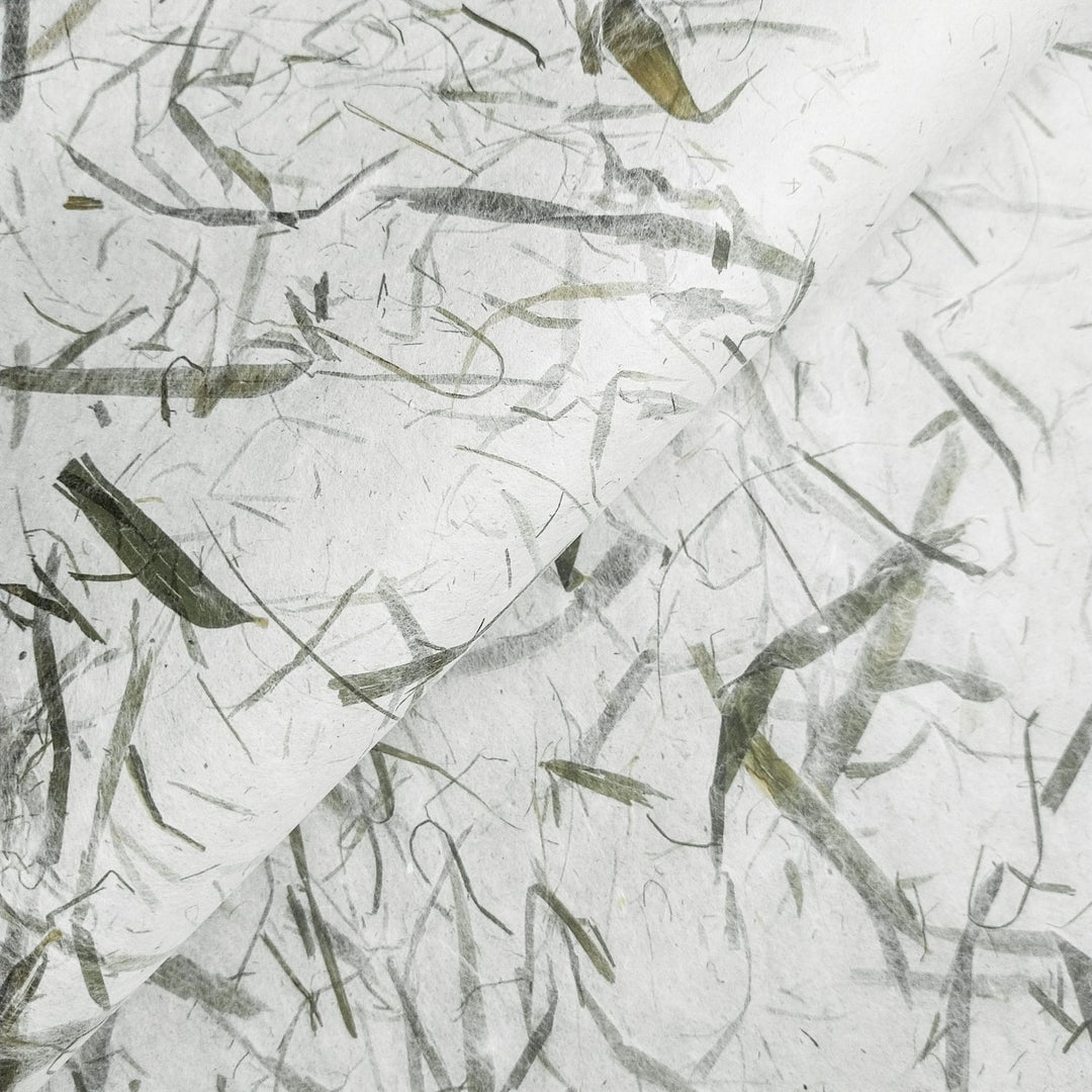 A close-up of Bamboo Leaf Kozo Paper from Kozo Studio showcases its textured, organic look with embedded bamboo leaves. The natural fold adds depth and dimension to the image.
