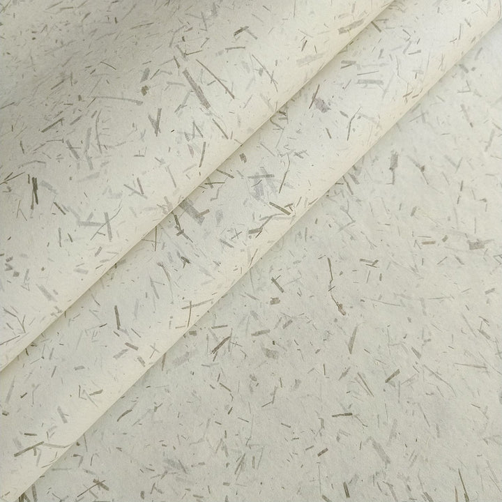 Close-up of Bamboo Confetti Kozo paper from Kozo Studio showing natural fibers and crushed bamboo leaves in beige and earthy tones, a strong and lightweight handmade mulberry paper.
