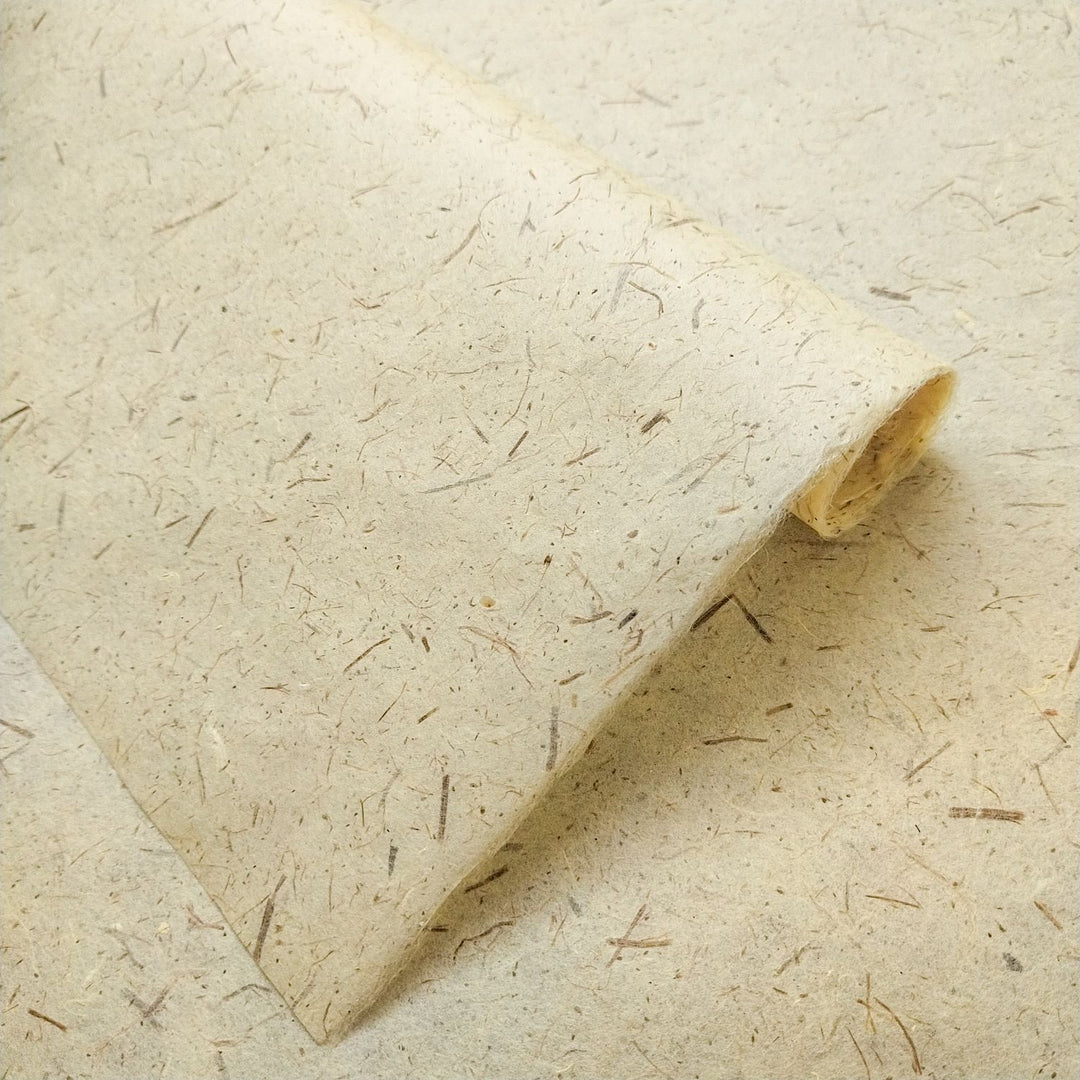 A close-up of Pine Leaf Kozo Paper by Kozo Studio, highlighting its textured beige surface with visible fibers and specks for an organic, natural look of handcrafted artistry.