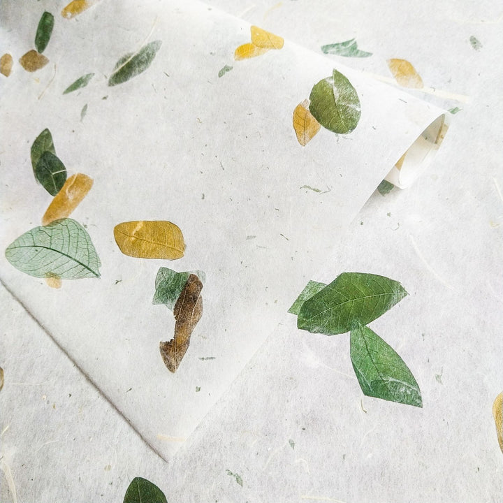 Artistic shot of Raintree Kozo paper from Kozo Studio, featuring a semi-transparent mulberry paper base with leaf accents in green and yellow hues.