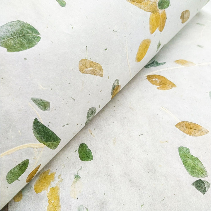 Close-up of Raintree Kozo Paper by Kozo Studio, featuring a textured surface with green and yellow leaves of different shapes and sizes. This handmade paper highlights its natural, artistic design.