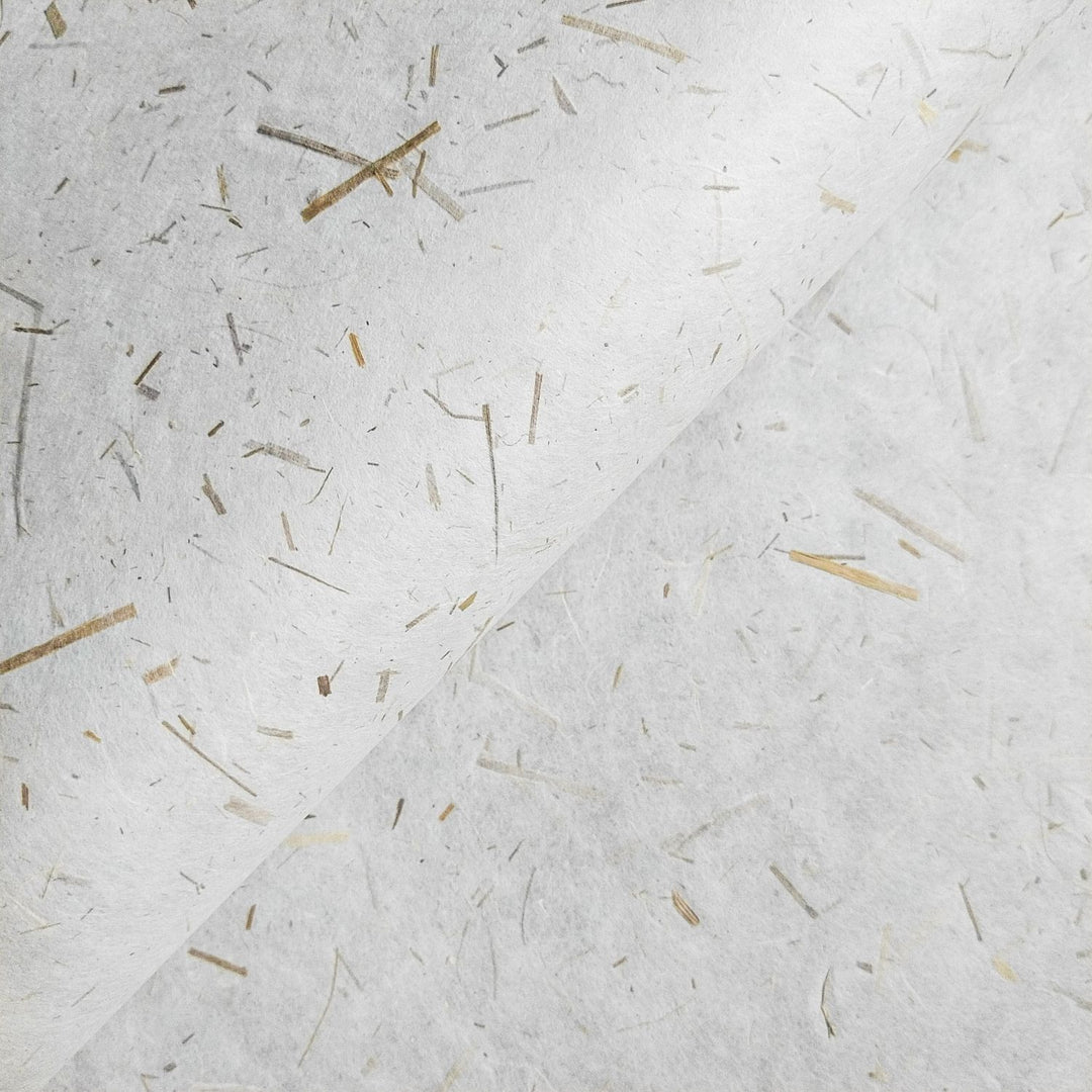 Close-up of Rice Straw Confetti Kozo Paper by Kozo Studio, showcasing its white handmade mulberry surface, with embedded fibers and straw-like lines. The papers slight curve in the upper half adds texture and depth.