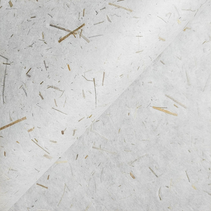 Close-up of Rice Straw Confetti Kozo Paper by Kozo Studio, showcasing its white handmade mulberry surface, with embedded fibers and straw-like lines. The papers slight curve in the upper half adds texture and depth.