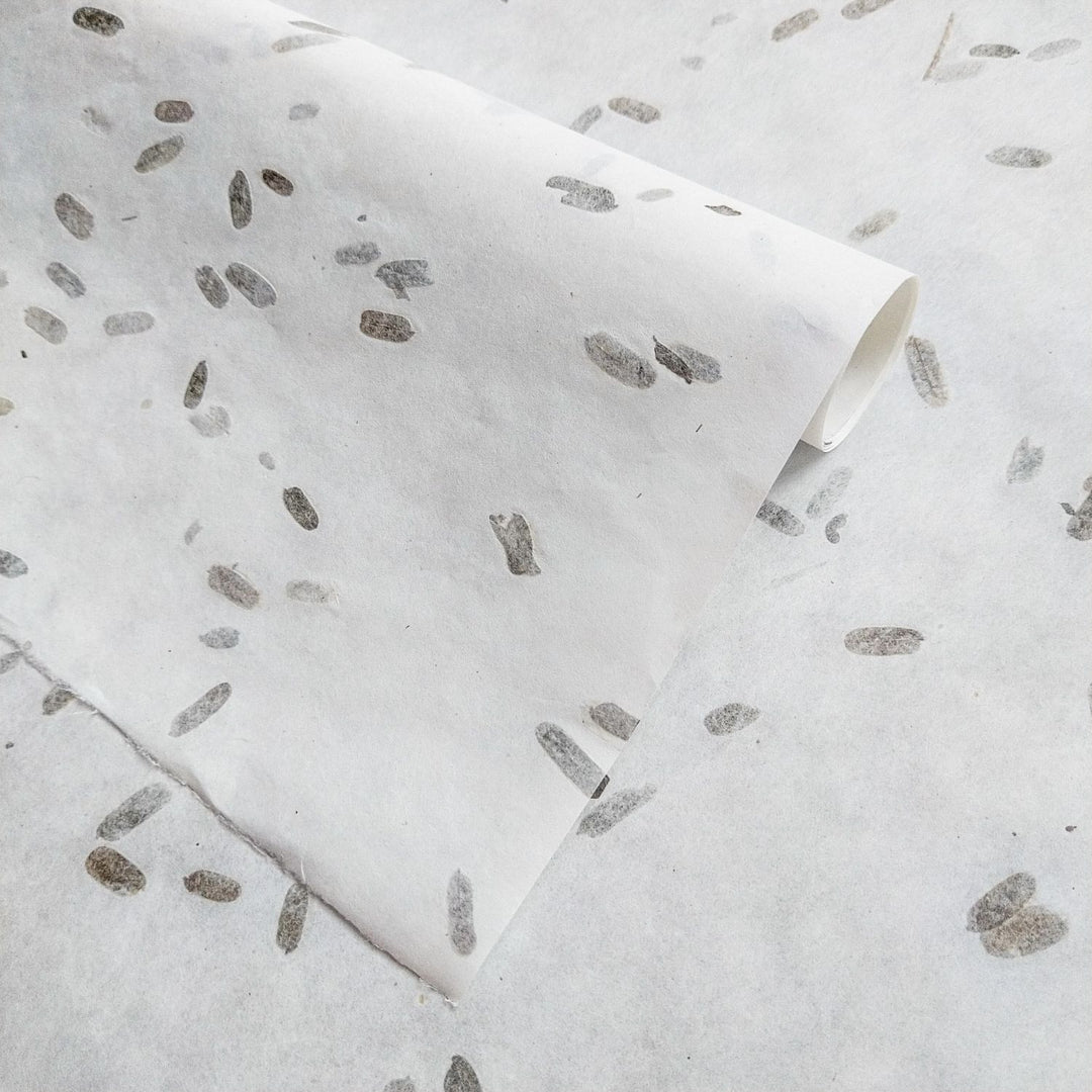 Decorative mulberry paper crafted by Kozo Studio, showcasing folded layers, tamarind leaf confetti, and a semi-transparent surface ideal for design projects.