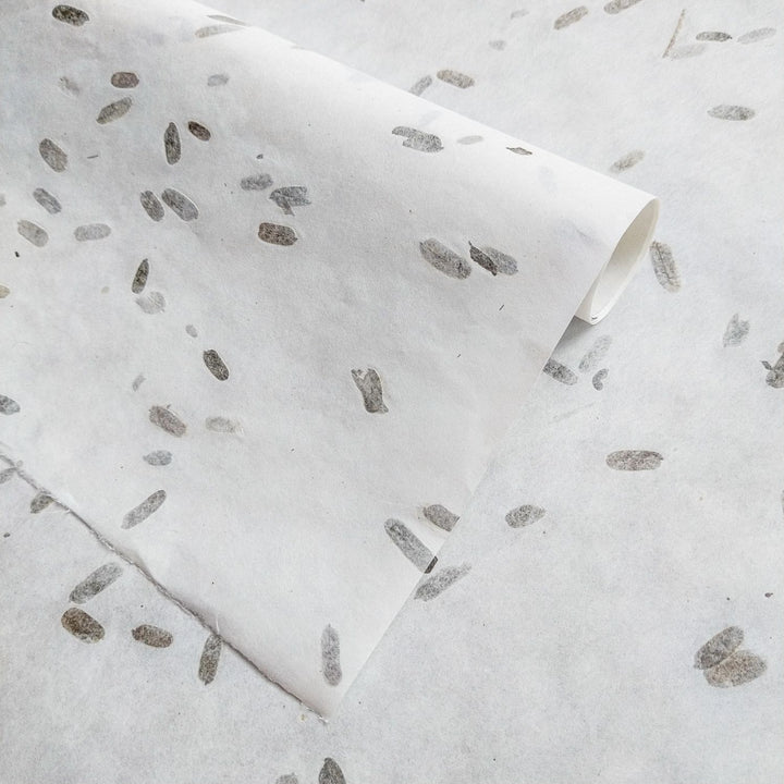 Decorative mulberry paper crafted by Kozo Studio, showcasing folded layers, tamarind leaf confetti, and a semi-transparent surface ideal for design projects.