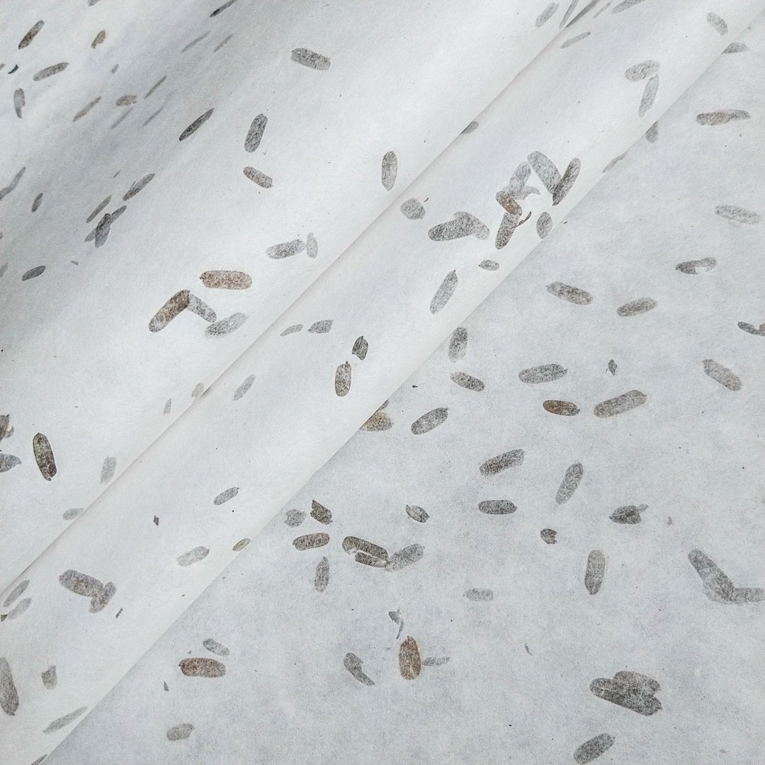 Close-up of mulberry paper by Kozo Studio, featuring handmade paper with tiny tamarind leaf inclusions for a natural, speckled pattern in gray and brown tones.