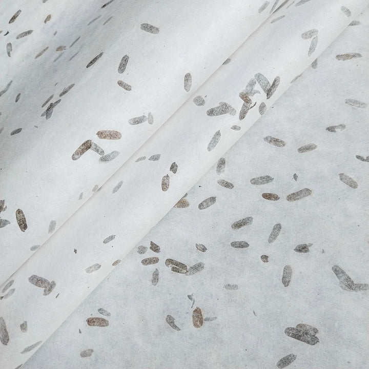 Close-up of mulberry paper by Kozo Studio, featuring handmade paper with tiny tamarind leaf inclusions for a natural, speckled pattern in gray and brown tones.