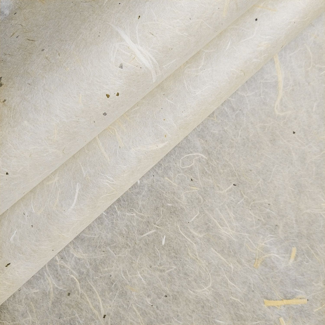 A close-up of Kozo Studios Unryu Kozo Paper with Mulberry Bark reveals its textured surface with visible fibers and small speckles. This handmade paper features a natural, off-white color, subtle variations, and a slightly rough texture for a soft, organic appearance enhanced by light and shadows.