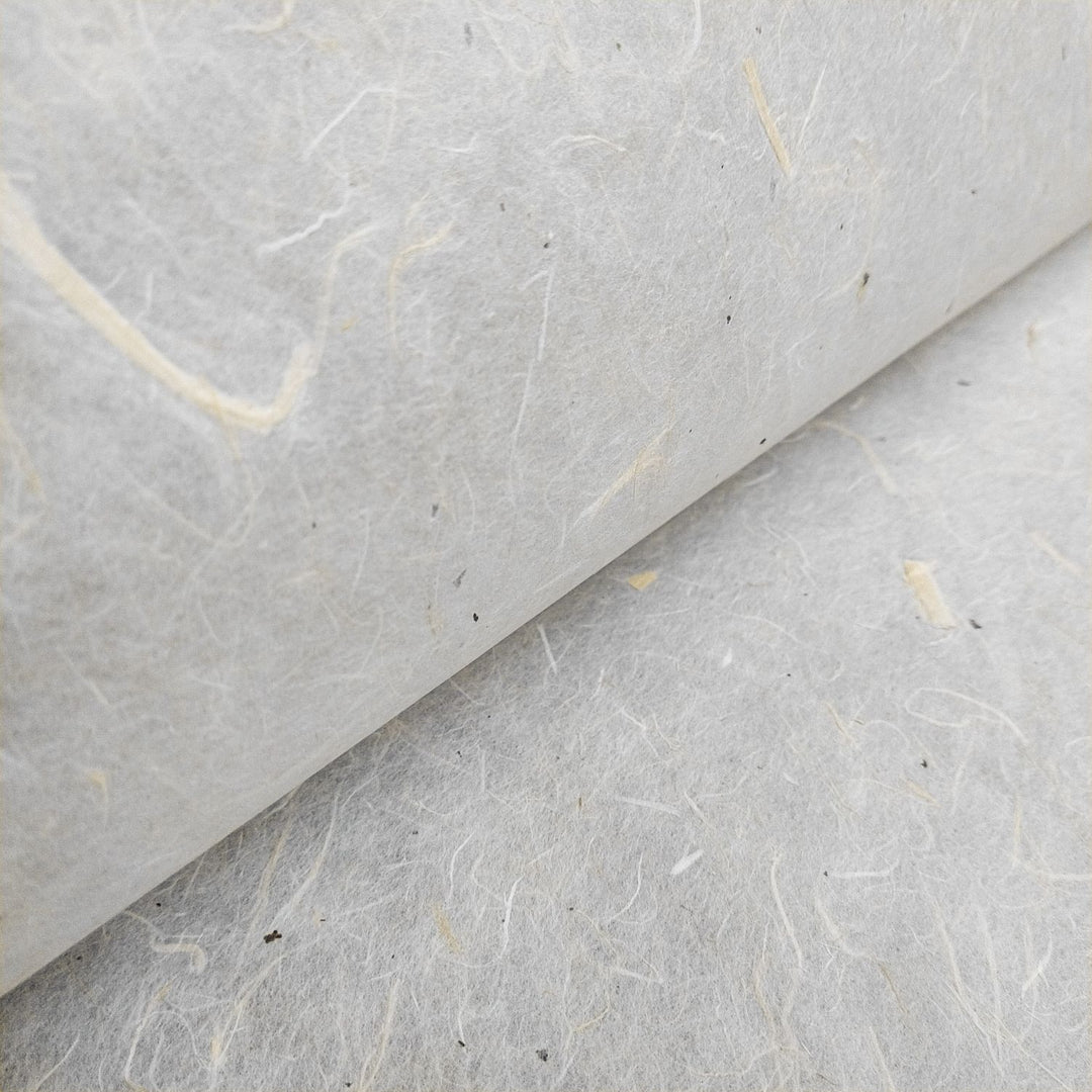 Close-up of Kozo Studios Unryu Kozo Paper with Mulberry Bark showcasing textured, fibrous off-white surface. Natural fibers and small flecks are visible, giving a rough and organic appearance that adds depth to the image.