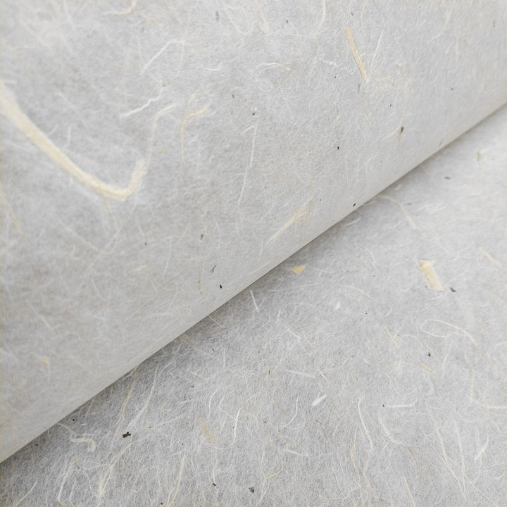 Close-up of Kozo Studios Unryu Kozo Paper with Mulberry Bark showcasing textured, fibrous off-white surface. Natural fibers and small flecks are visible, giving a rough and organic appearance that adds depth to the image.