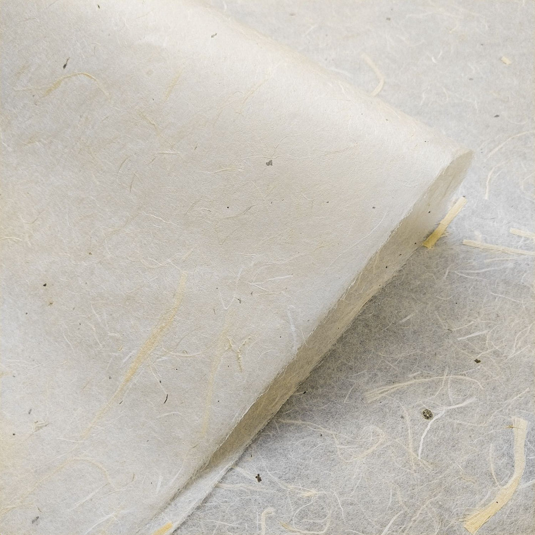 A close-up of Unryu Kozo Paper with Mulberry Bark by Kozo Studio shows its textured, fibrous mulberry composition in light beige tones. The papers corner is rolled, highlighting its thickness and interwoven natural fibers.