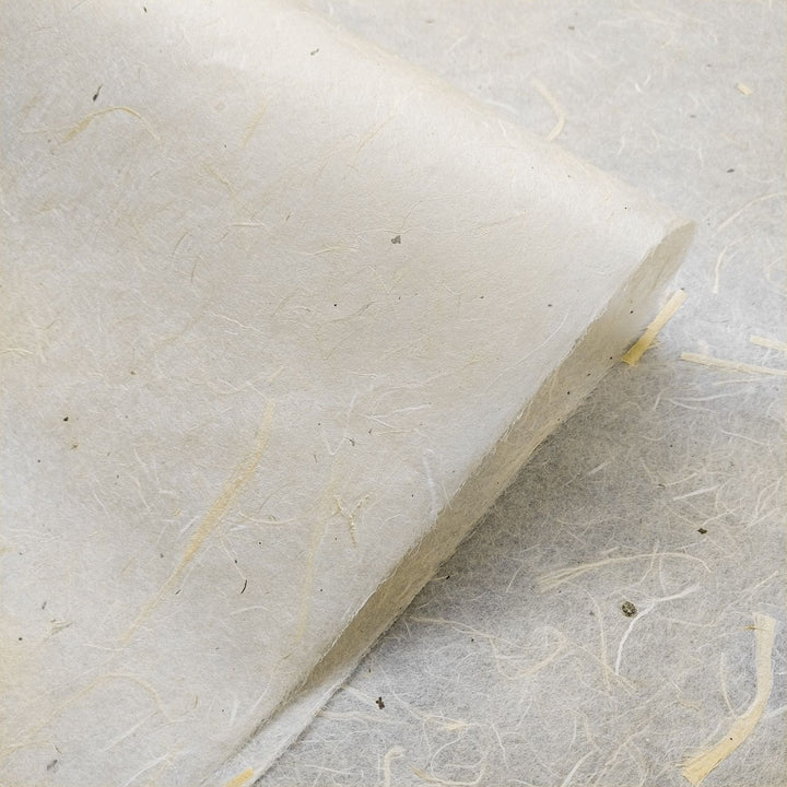 A close-up of Unryu Kozo Paper with Mulberry Bark by Kozo Studio shows its textured, fibrous mulberry composition in light beige tones. The papers corner is rolled, highlighting its thickness and interwoven natural fibers.