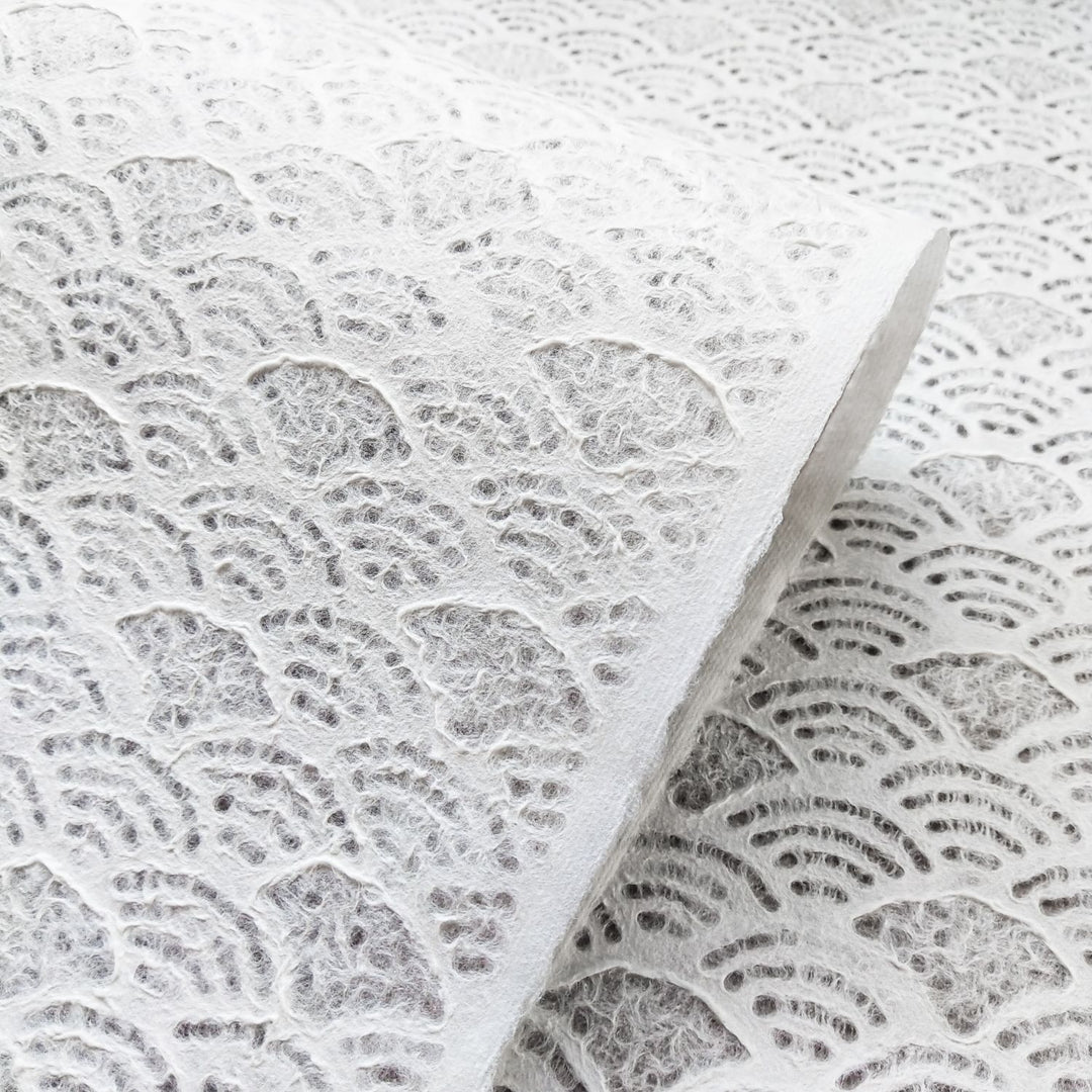 The intricate, lace-like design of Kozo Studios Handmade Lace Kozo Paper (Fan) showcases a delicate, elegant surface with semi-circular wave patterns on textured white mulberry paper.