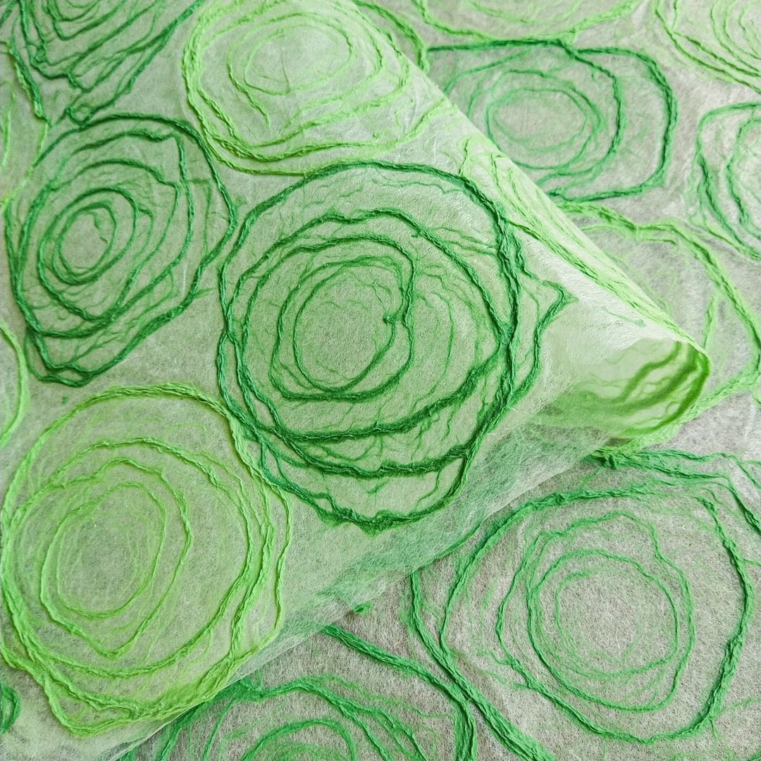 Close-up of translucent handmade paper from Kozo Studio, made with mulberry pulp in a rose pattern of green hues, ideal for artistic or decorative use.