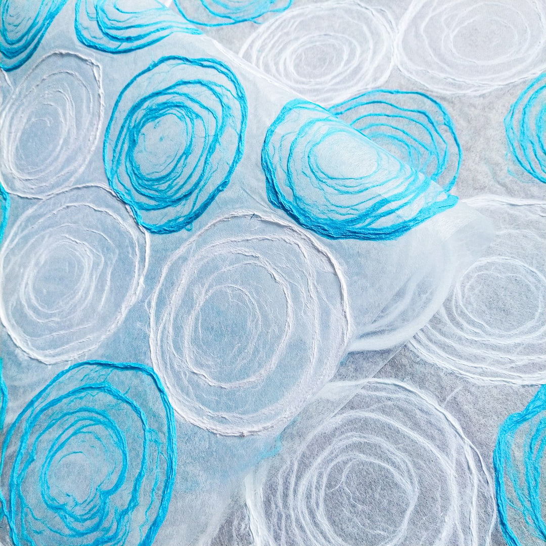 A sheet of translucent handmade mulberry paper with soft blue and white tones, showcasing hand-applied pulp circles from Kozo Studio's collection.