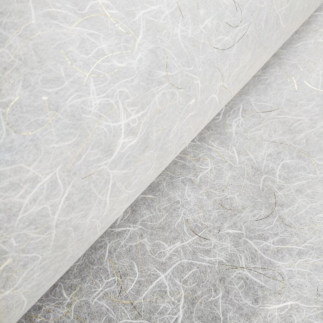 Close-up of Kozo Studios Golden Tinsel Unryu Kozo Paper (White) reveals a textured, fibrous surface with thin, irregular strands in varied shades and subtle gold accents. It appears delicate and slightly translucent, suggesting an artisanal quality of traditional Mulberry papermaking techniques.