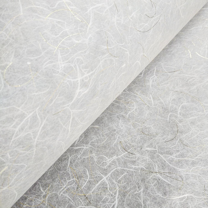 Close-up of Kozo Studios Golden Tinsel Unryu Kozo Paper (White) reveals a textured, fibrous surface with thin, irregular strands in varied shades and subtle gold accents. It appears delicate and slightly translucent, suggesting an artisanal quality of traditional Mulberry papermaking techniques.