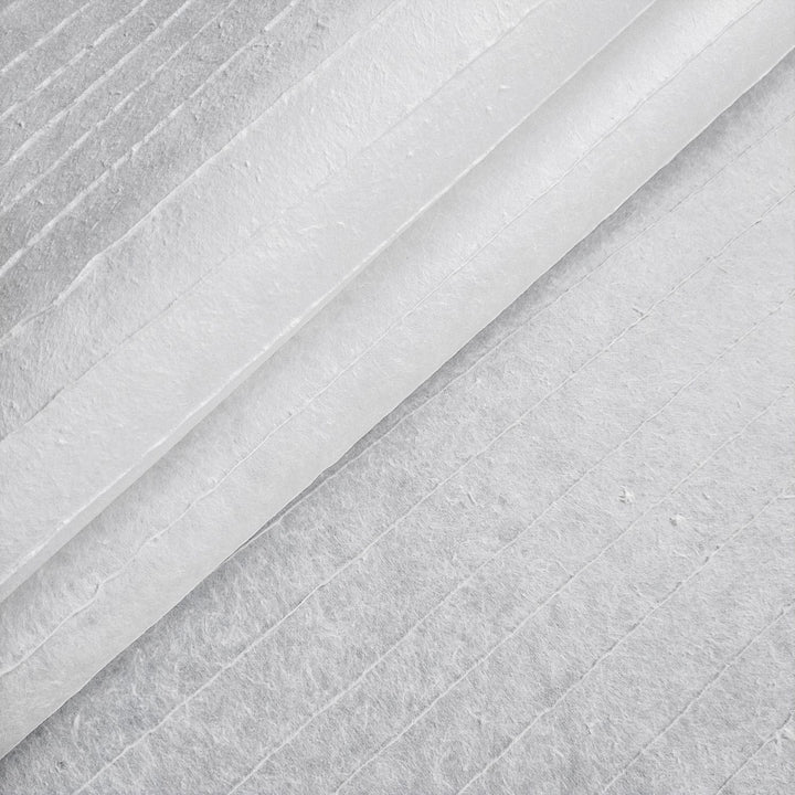 Close-up of Handmade Stripe Marking Kozo Paper (White) by Kozo Studio, featuring textured sheets stacked diagonally. Fibrous surface with subtle vertical lines forms an abstract pattern, and the top sheet is slightly lifted to reveal layers underneath.