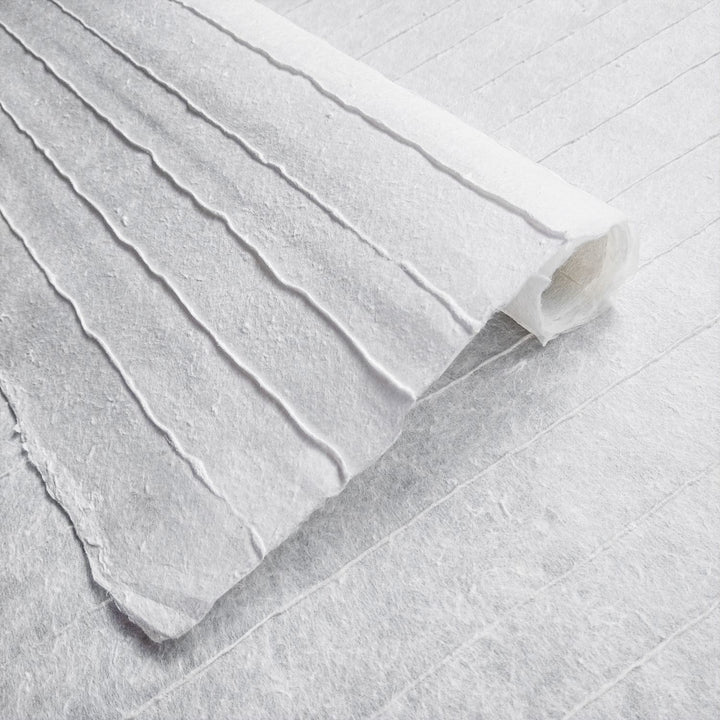 A close-up of Handmade Stripe Marking Kozo Paper (White) by Kozo Studio reveals its white textured surface with raised, parallel lines and fibrous detail, echoing traditional craftsmanship.