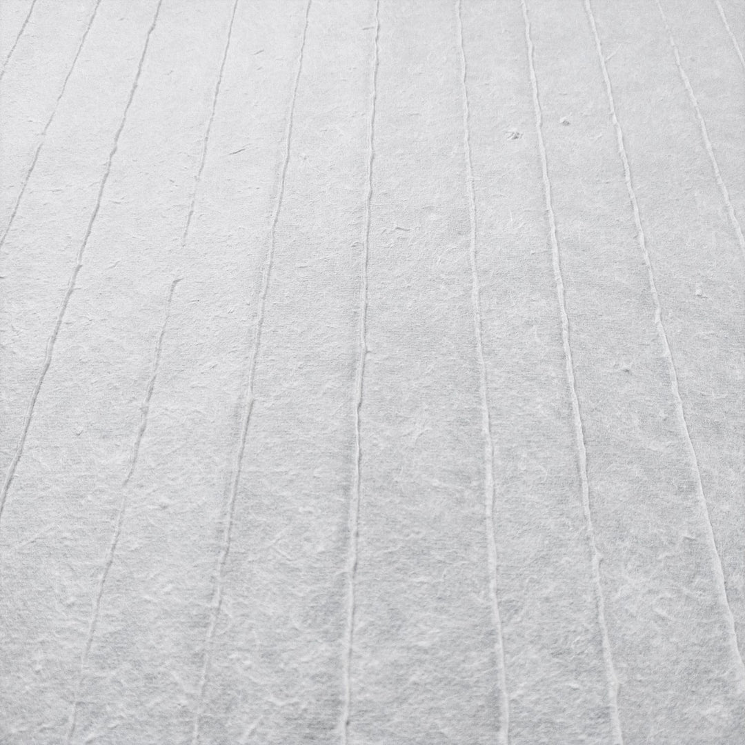 The close-up of Kozo Studios Handmade Stripe Marking Kozo Paper (White) reveals a soft, fabric-like texture with faint, evenly spaced parallel lines. A subtle grid pattern adds depth and simplicity, while muted tones evoke an elegant tranquility reminiscent of rice paper.