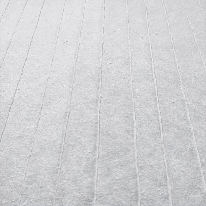The close-up of Kozo Studios Handmade Stripe Marking Kozo Paper (White) reveals a soft, fabric-like texture with faint, evenly spaced parallel lines. A subtle grid pattern adds depth and simplicity, while muted tones evoke an elegant tranquility reminiscent of rice paper.