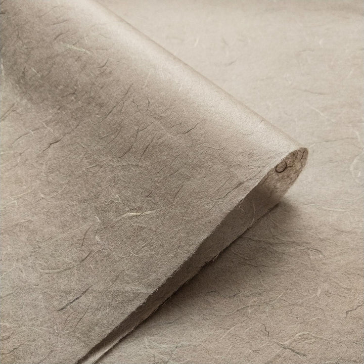 A close-up of a sheet of Kozo Studios Unryu Kozo Paper (Grey), textured and slightly curled at one corner, showcasing its fibrous appearance with visible uneven fibers and a rough surface.
