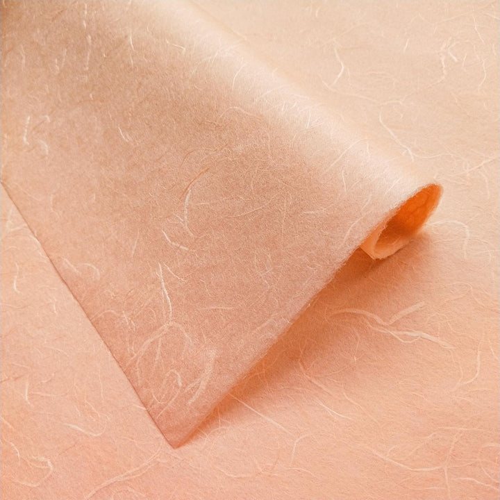Salmon orange Unryu Kozo paper by Kozo Studio with delicate mulberry fibers and organic folds creating soft shadows.