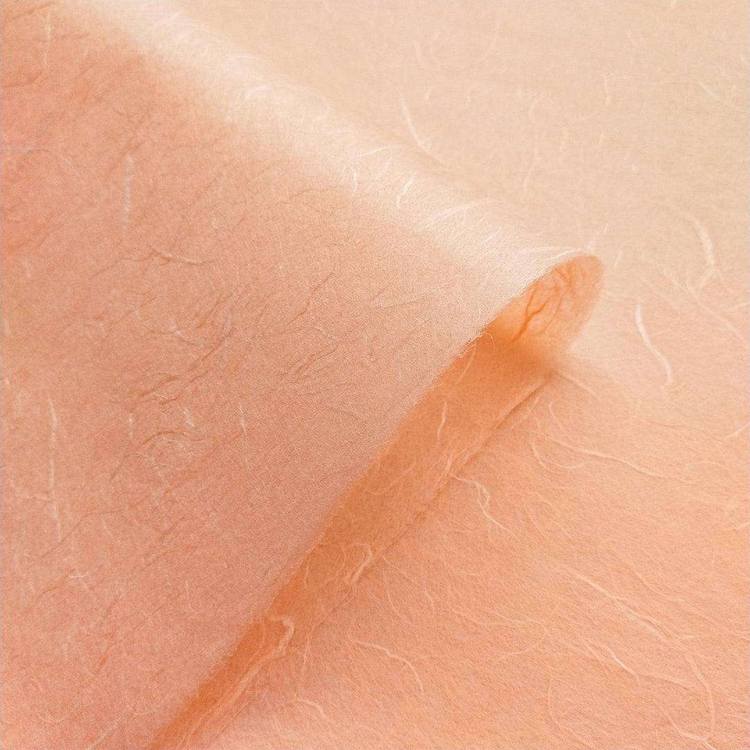 Handmade mulberry paper from Kozo Studio shown in salmon orange, with translucent fibers and subtle tonal shifts.