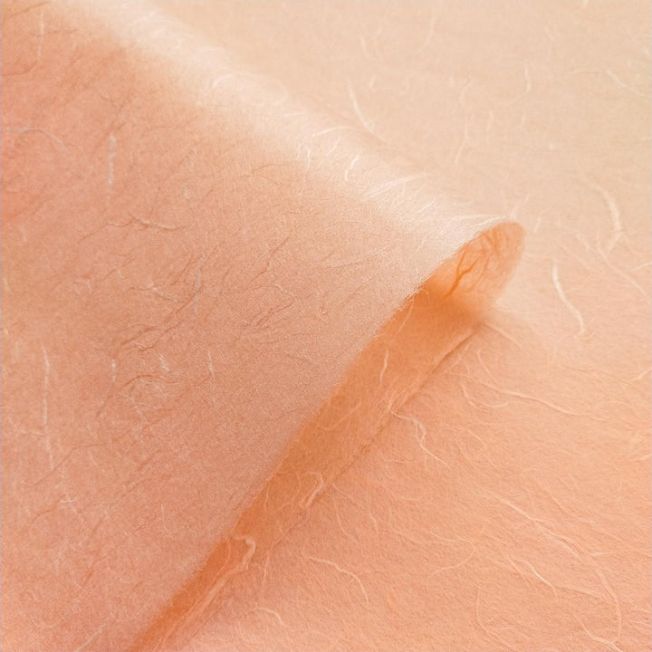 Handmade mulberry paper from Kozo Studio shown in salmon orange, with translucent fibers and subtle tonal shifts.