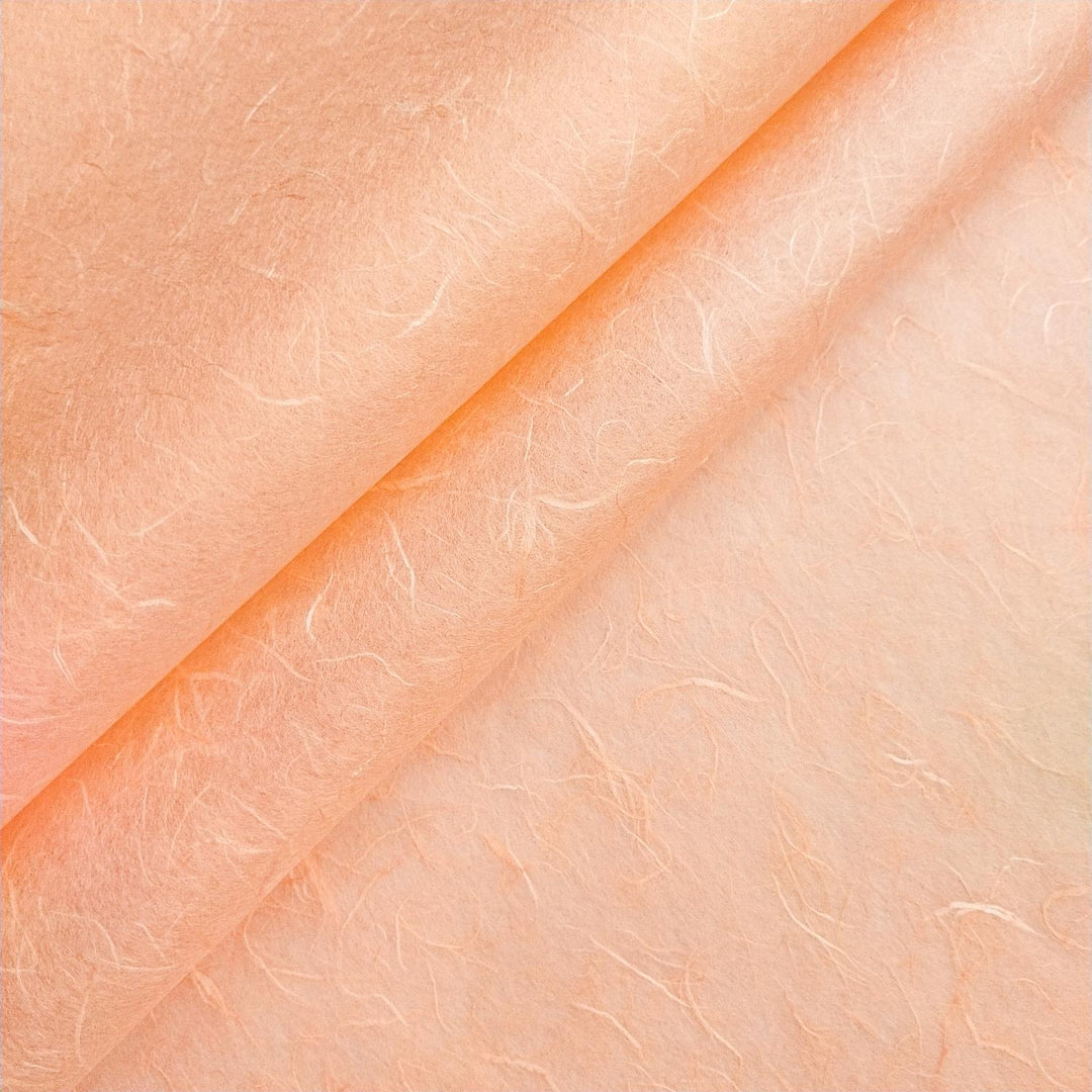 Close-up of Kozo Studio handmade paper in salmon orange, featuring visible mulberry fibers and natural texture variations.