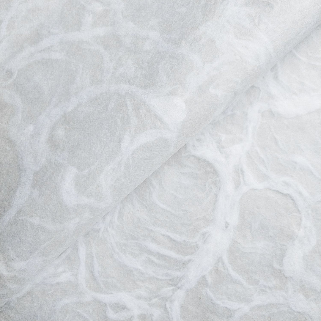 Close-up of white Ripple mulberry paper by Kozo Studio, showcasing a delicate handmade paper texture with fibrous swirls resembling rippling water.