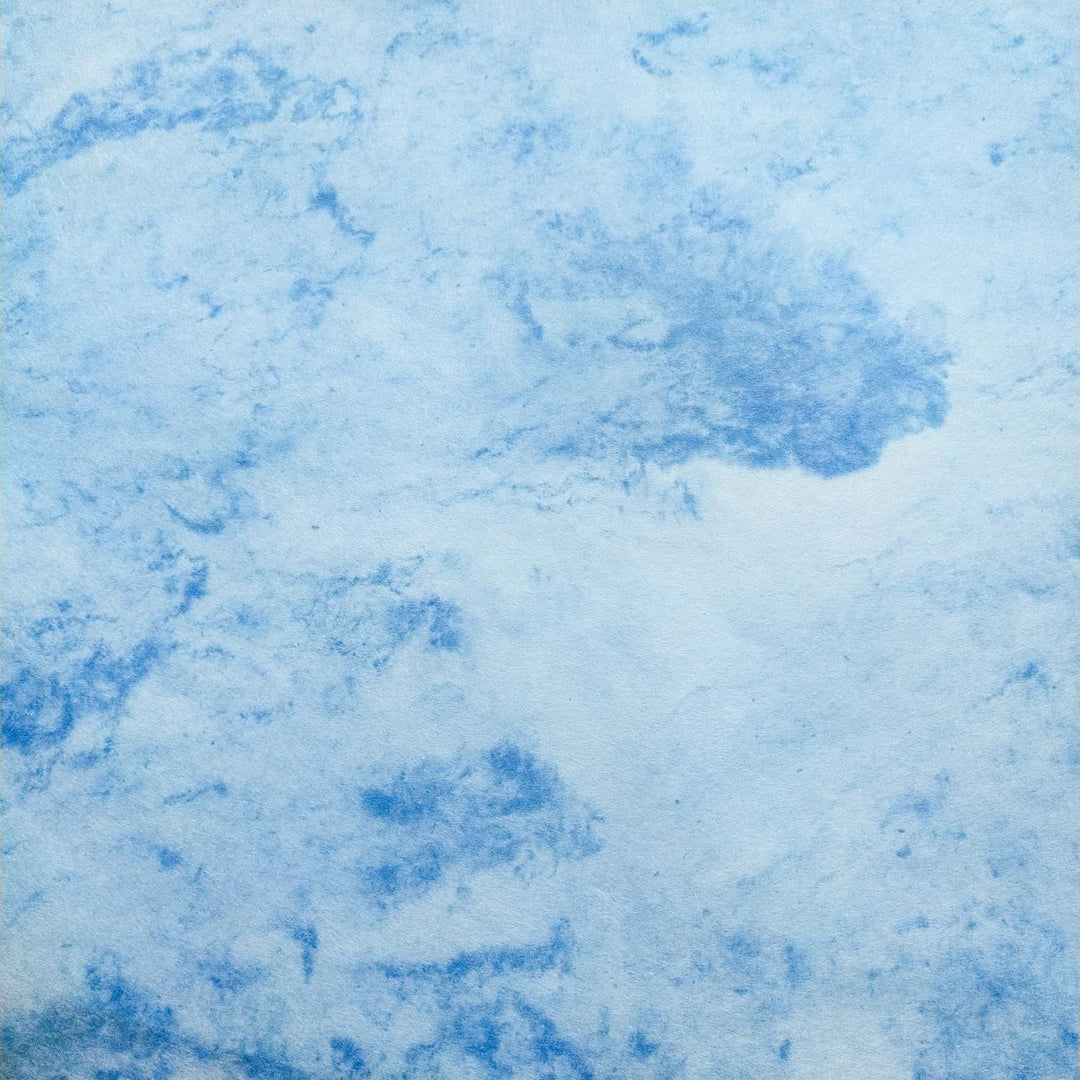Handmade paper from Kozo Studio showing a serene blend of blue and white swirls on textured mulberry paper, gently folded in the center.