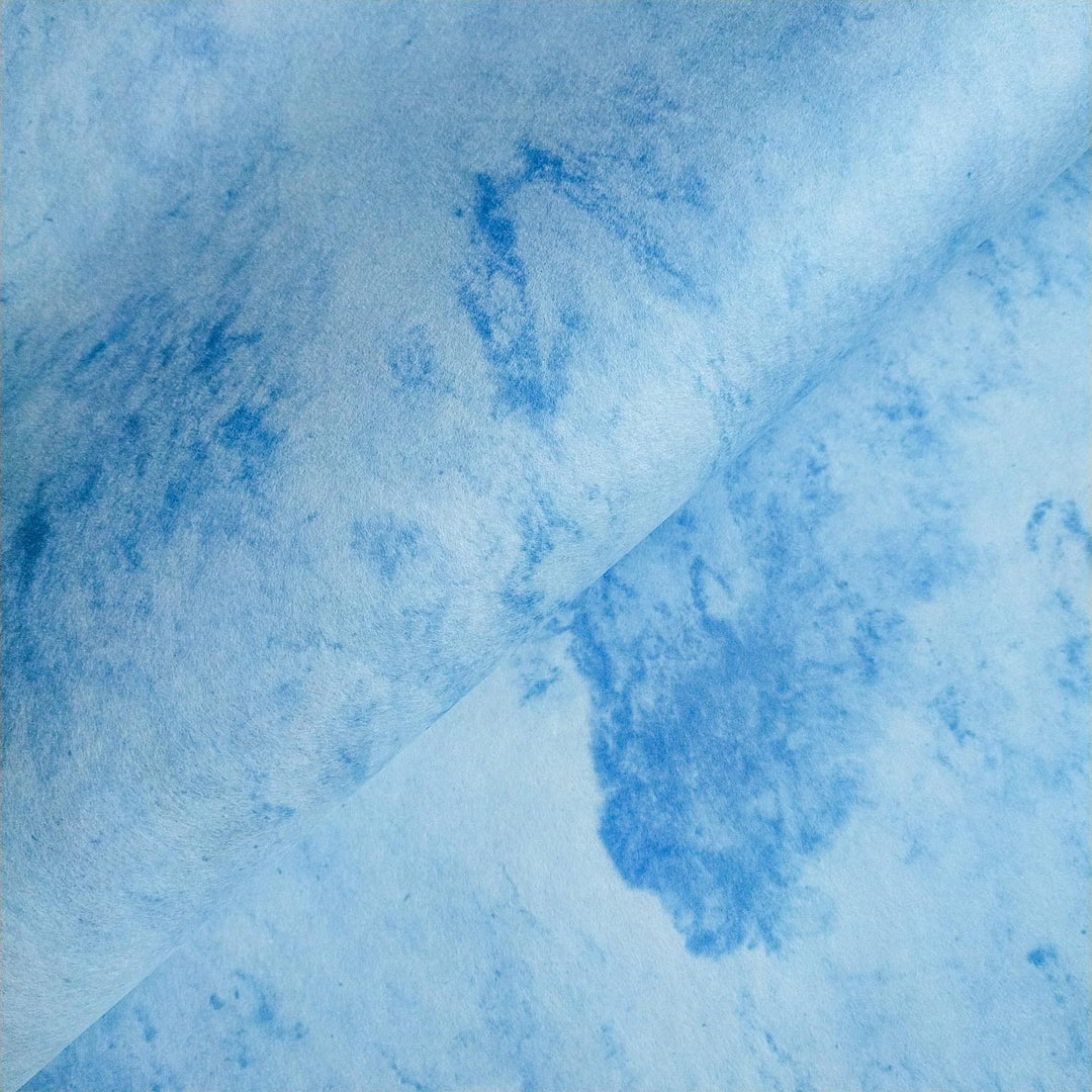 Close-up of Sky Kozo Paper Design 1 by Kozo Studio featuring marbled sky-blue handmade paper with delicate white swirls and a soft fold in the center.