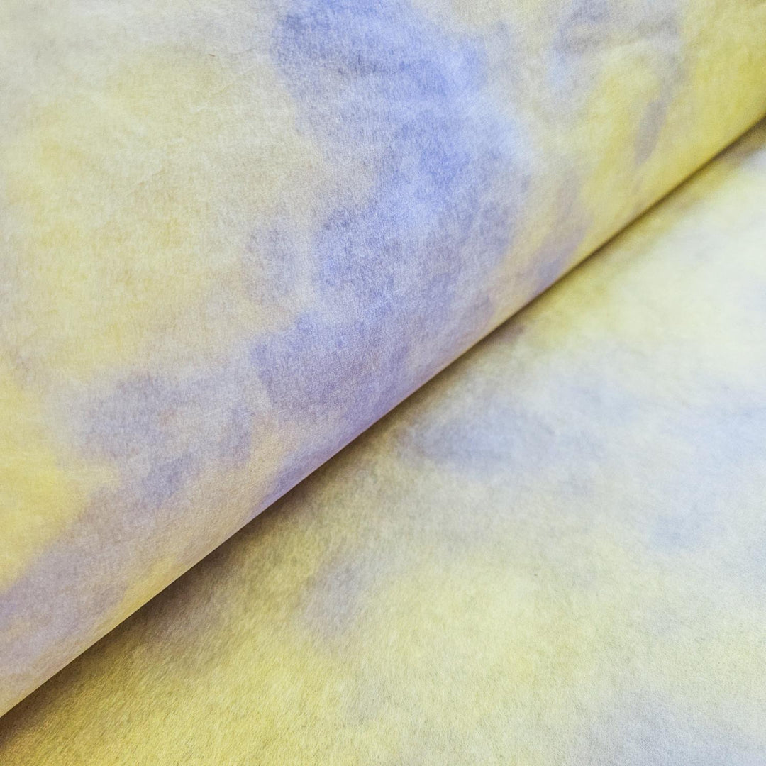 A close-up of Ombre Kozo Mulberry Paper (#3 Canary Glow) from Kozo Studio reveals a smooth, cloud-like pattern with a gradient of soft yellow and gentle blue shades that blend subtly.