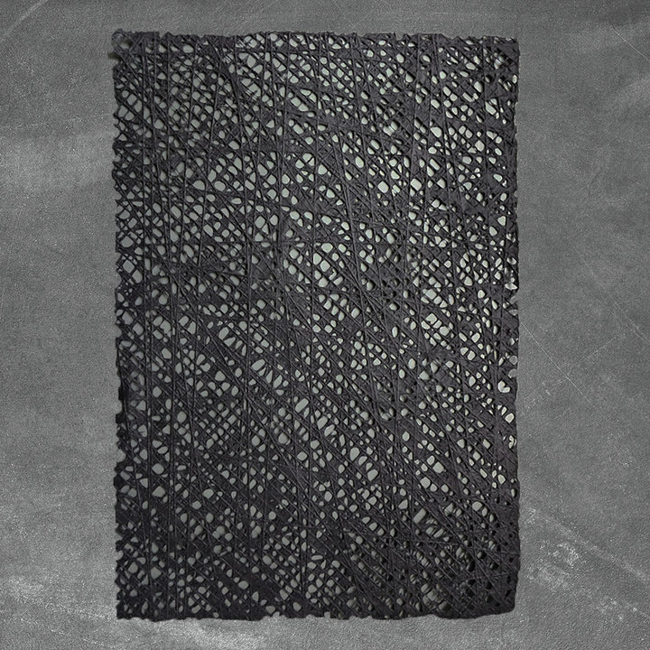 Kozo Studio's handmade paper sheet in black, showcasing a unique fishnet pattern made from cotton threads layered over traditional mulberry pulp.