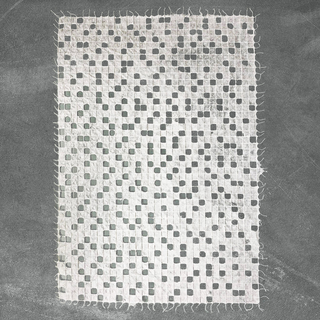 The Handmade Kobe Kozo Paper by Kozo Studio is a textured white mulberry paper with a grid-like pattern of small holes. Its edges are slightly frayed and it is set against a dark background.