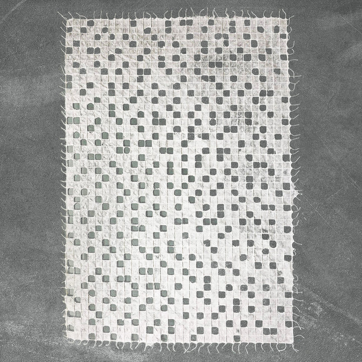 The Handmade Kobe Kozo Paper by Kozo Studio is a textured white mulberry paper with a grid-like pattern of small holes. Its edges are slightly frayed and it is set against a dark background.