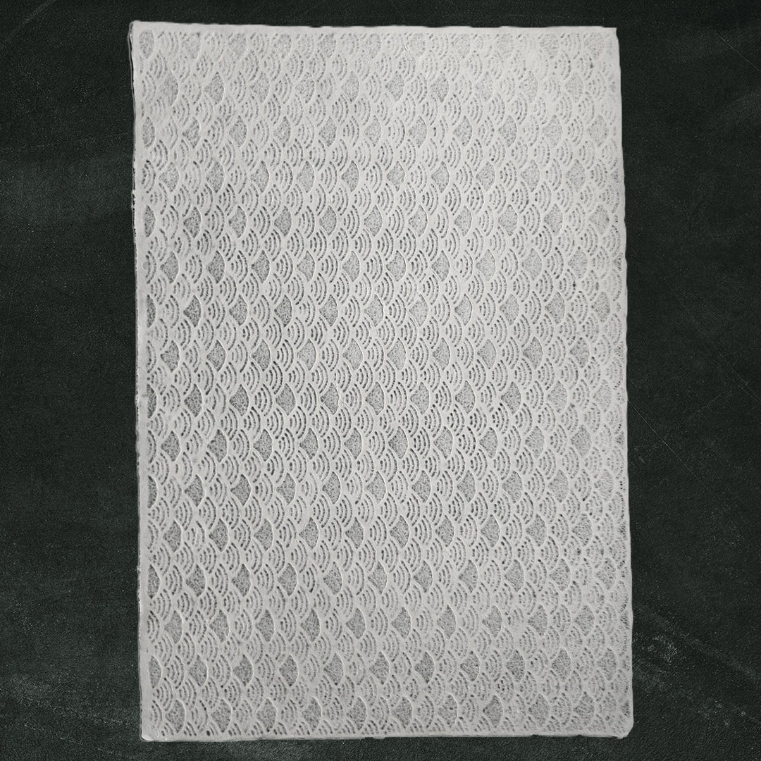 The Handmade Lace Kozo Mulberry Paper (Fan) by Kozo Studio is showcased on a dark green background, with its wavy, intricate pattern of delicate rice paper.