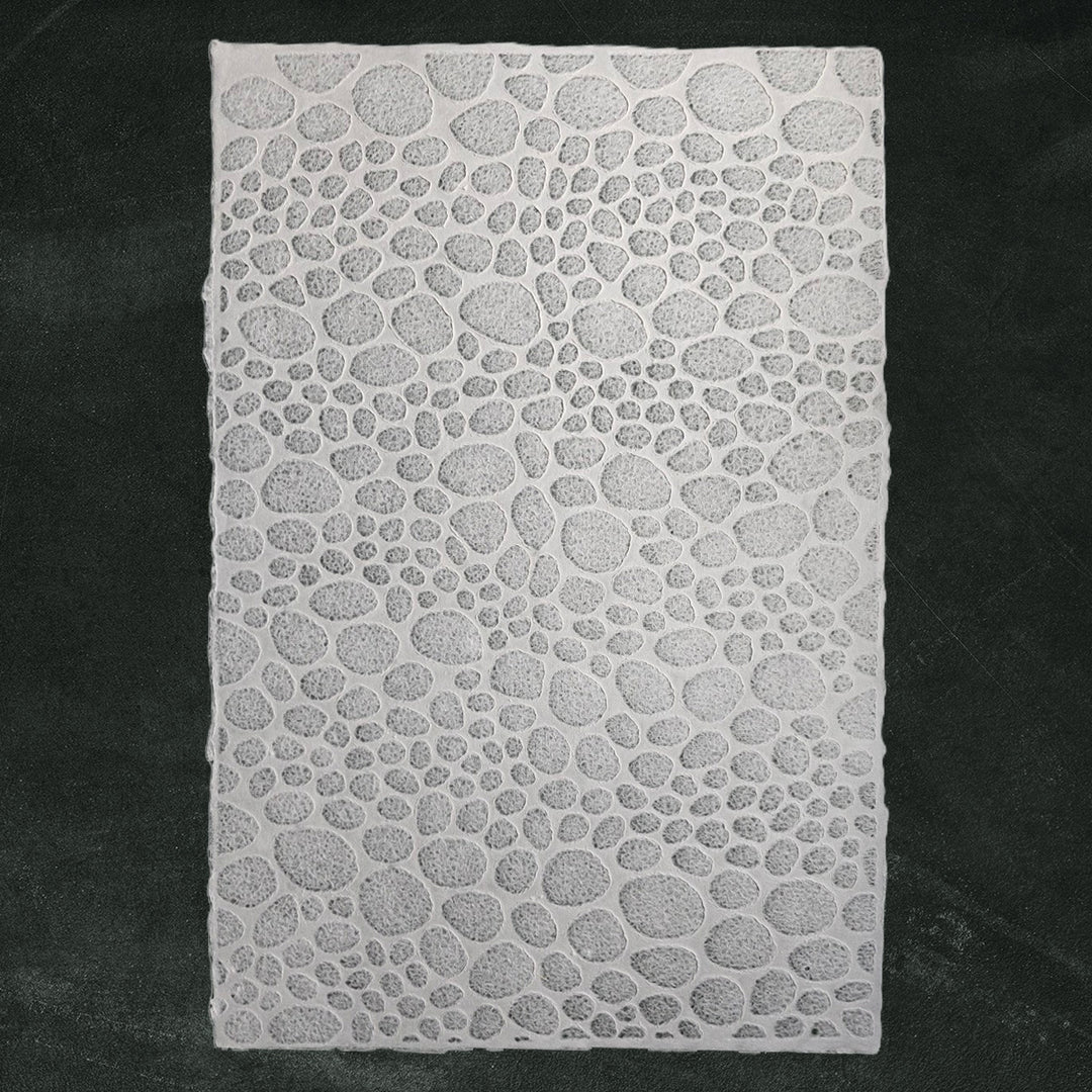 Intricate handmade paper from Kozo Studio showing lace-like stone patterns, made from mulberry fibers using water displacement for a translucent finish.